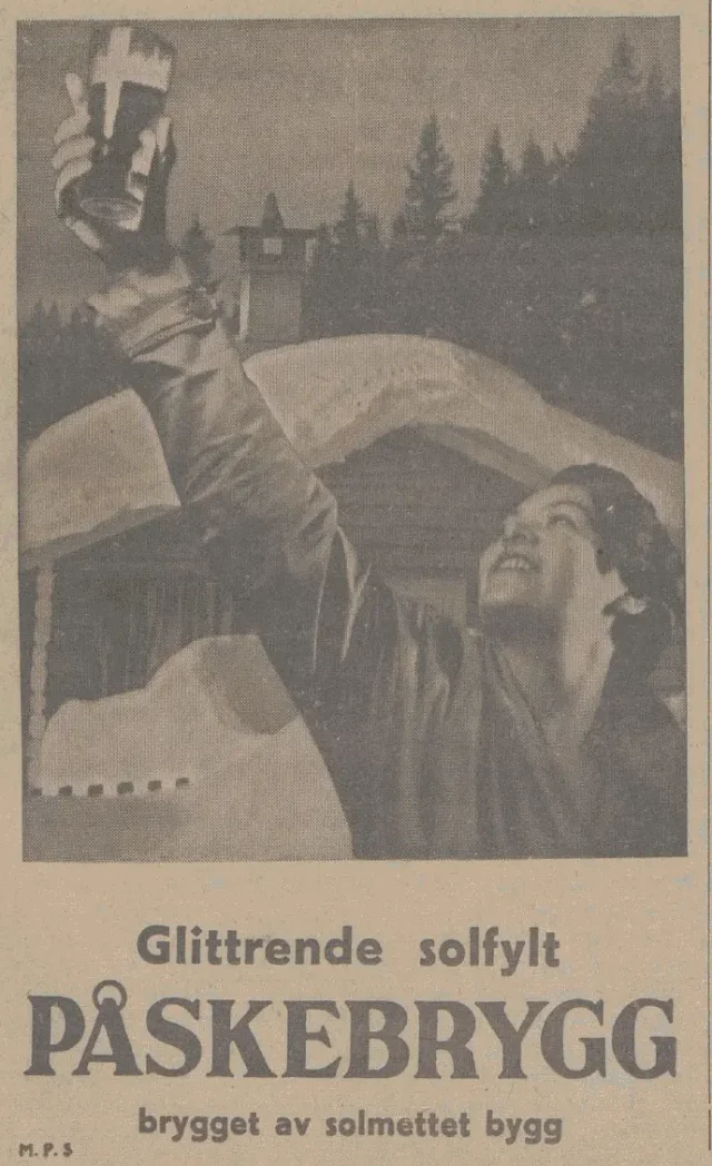 En dame på en snødekt hytte strekker ut armen med et glass påskebrygg og skåler mot sola